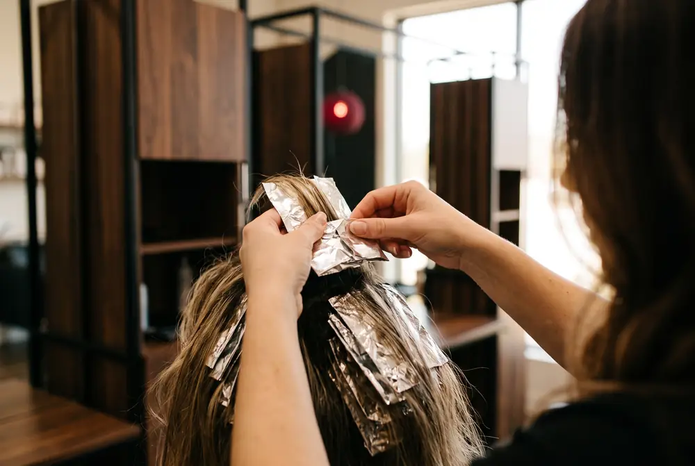 Manos de una estilista doblando un papel de aluminio sobre un mecho&oacute;n de pelo, vistas desde atr&aacute;s